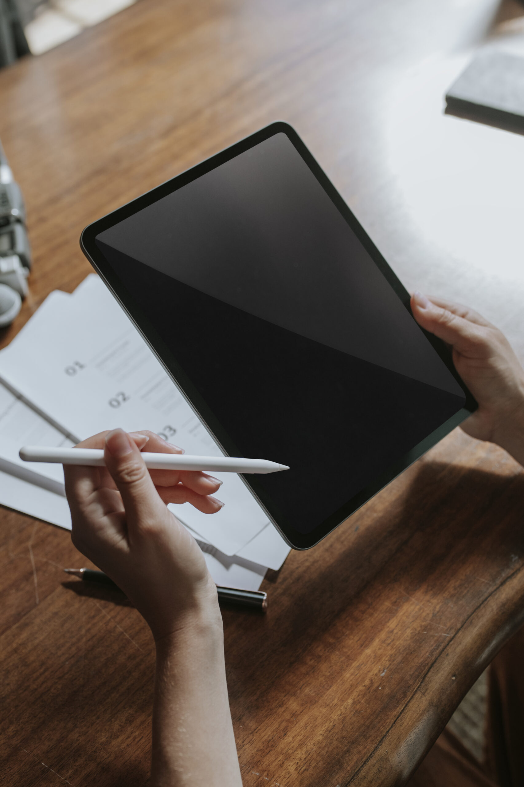 Mains tenant une tablette et un stylet sur un bureau en bois